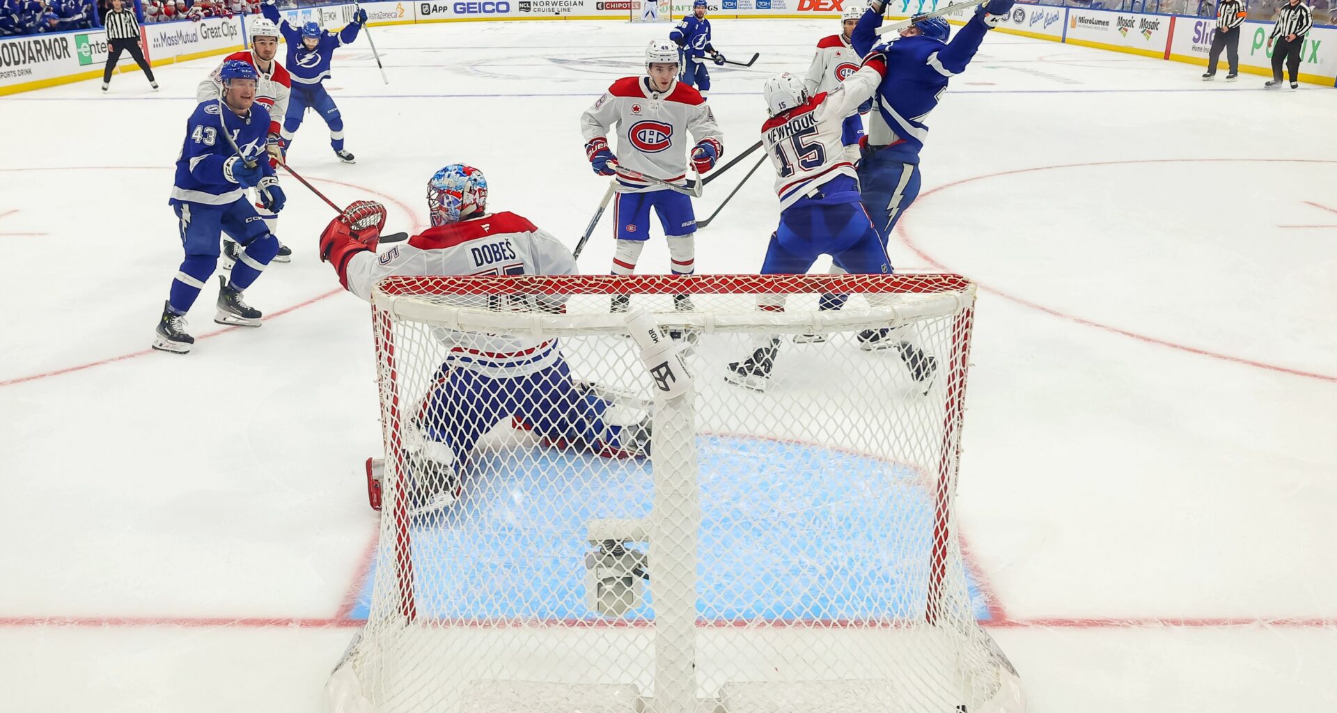Tampa Bay Lightning players raise their arms in celebration as the puck is in the net behind the Canadiens goaltender, in a photo from behind the net.