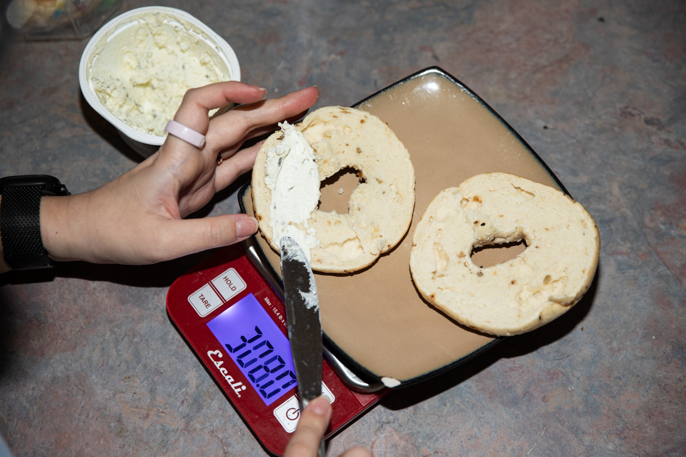 Top-down view of senior reviewer Victoria Song’s hands while weighing a bagel on a food scale
