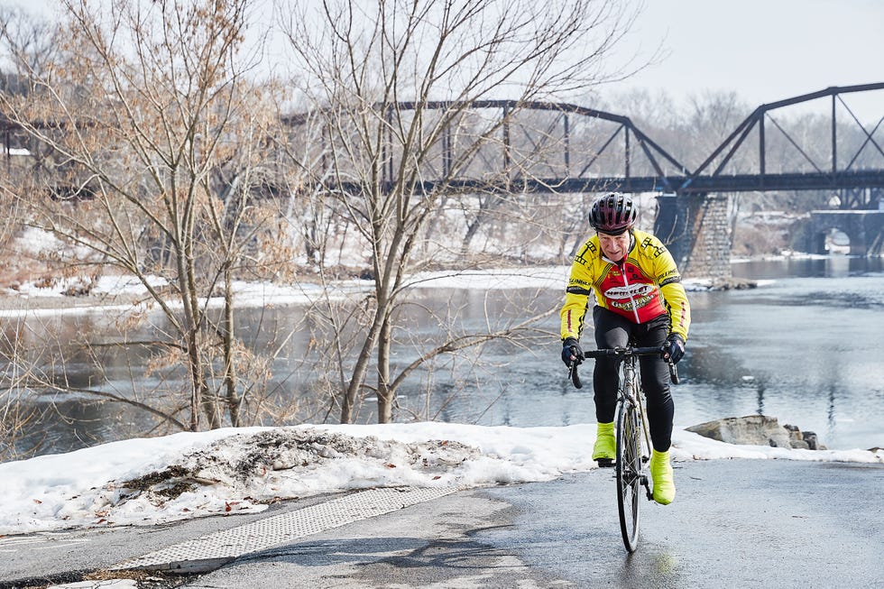 Cyclist riding along a winter riverbank with bare trees and snow. Cyclist riding along a winter riverbank with bare trees and snow.
