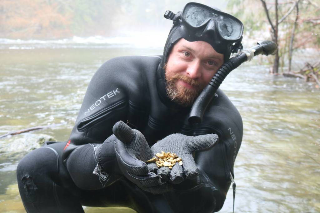 Paul Larouche stands in Sooke River with a handful of gold he has previously found. (Ben Fenlon/Sooke News Mirror)