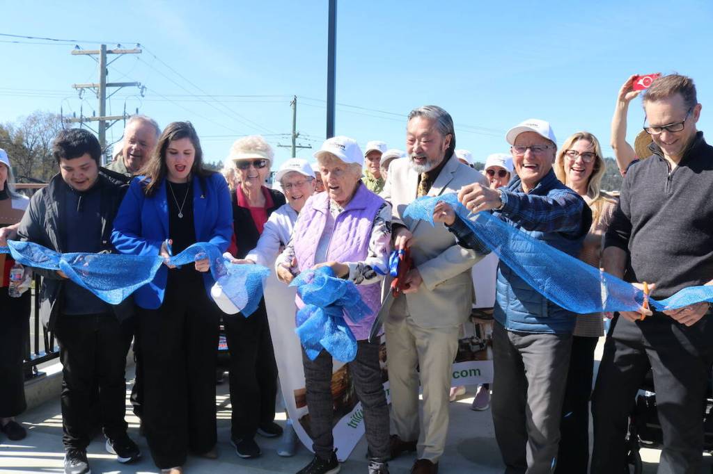 Songhees Coun. Eugene Sam, Esquimalt-Colwood MLA Darlene Rochford, and Mayor Doug Kobayashi cut the ribbon with the help of West Shore Village seniors at the official opening of the Galloping Goose pedestrian and cycling bridge. (Ben Fenlon/Goldstream Gazette)