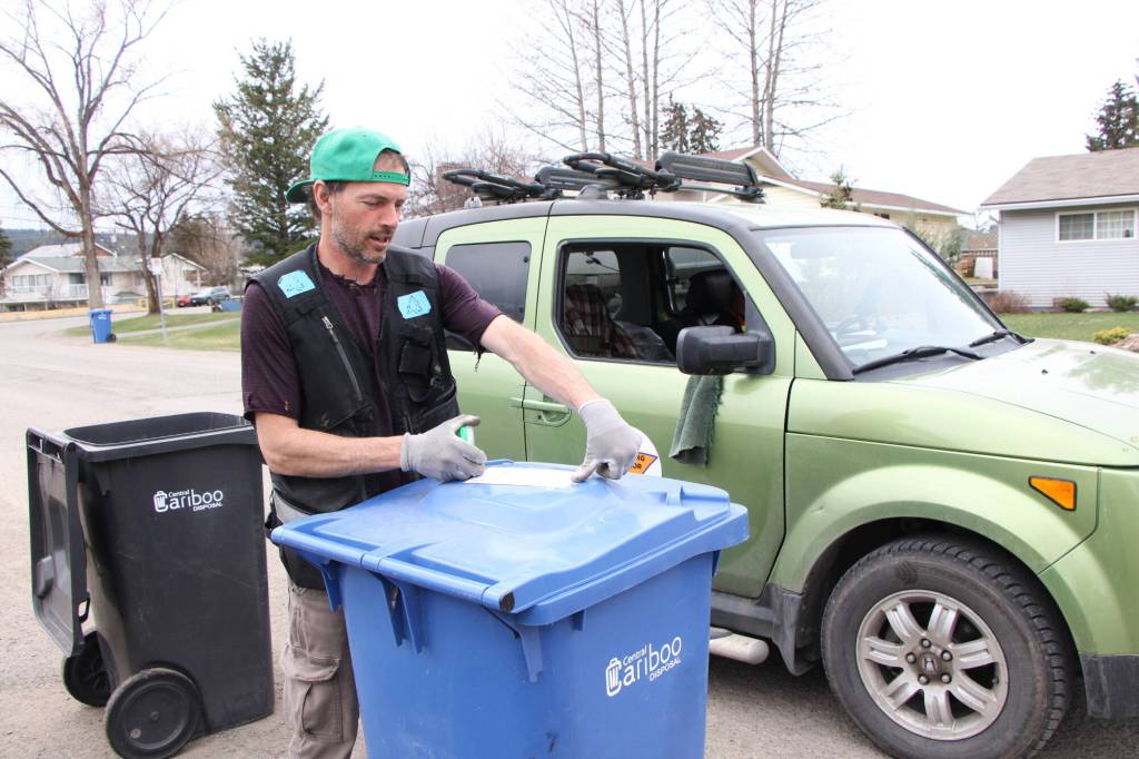 Oliver Berger attaches an Oops Card to a recycling bin in 100 Mile House. (Patrick Davies photo - 100 Mile Free Press)