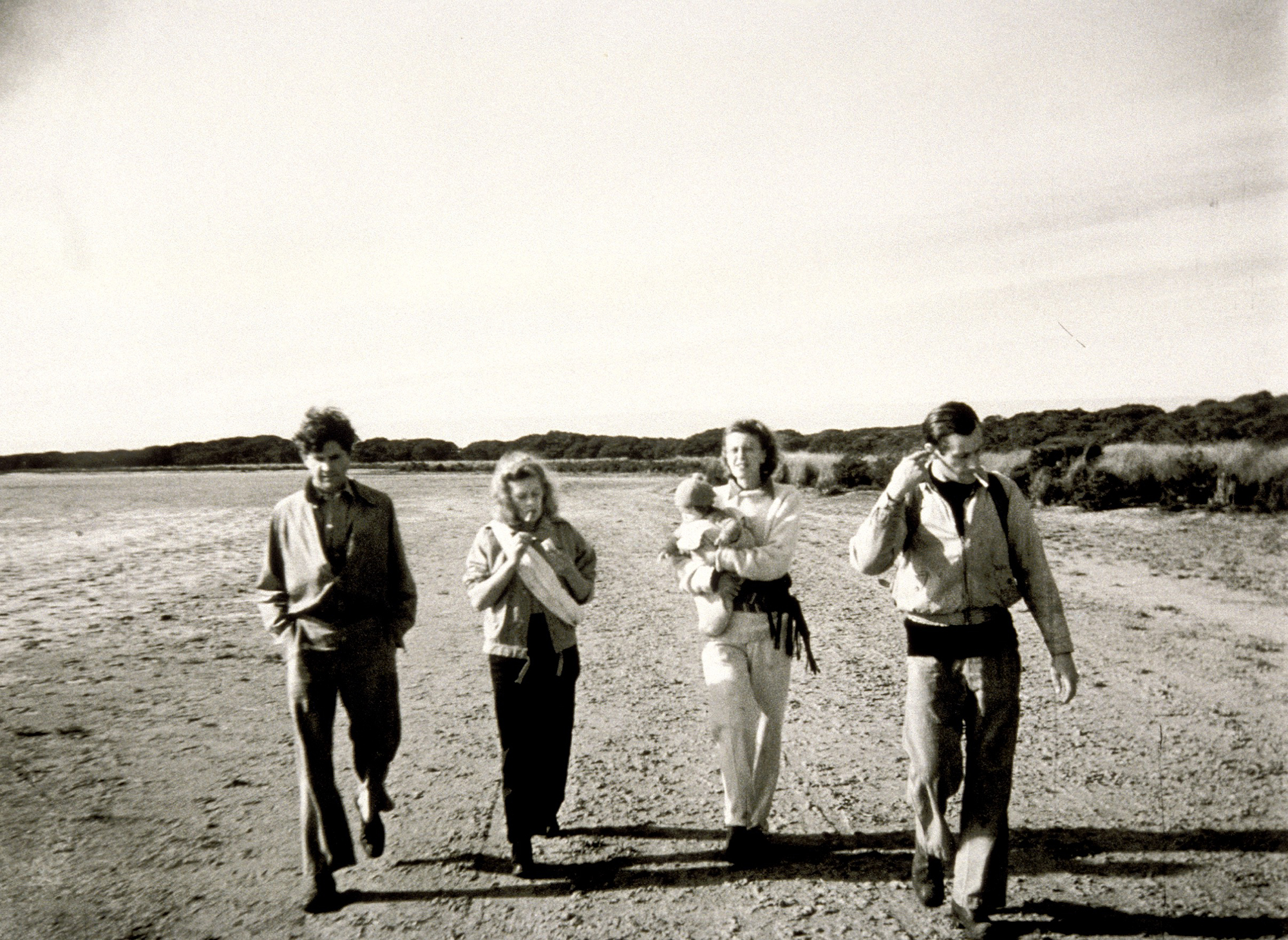 A black and white photograph of four people, one carrying a baby, walking side-by-side in a country landscape in the 1940s.