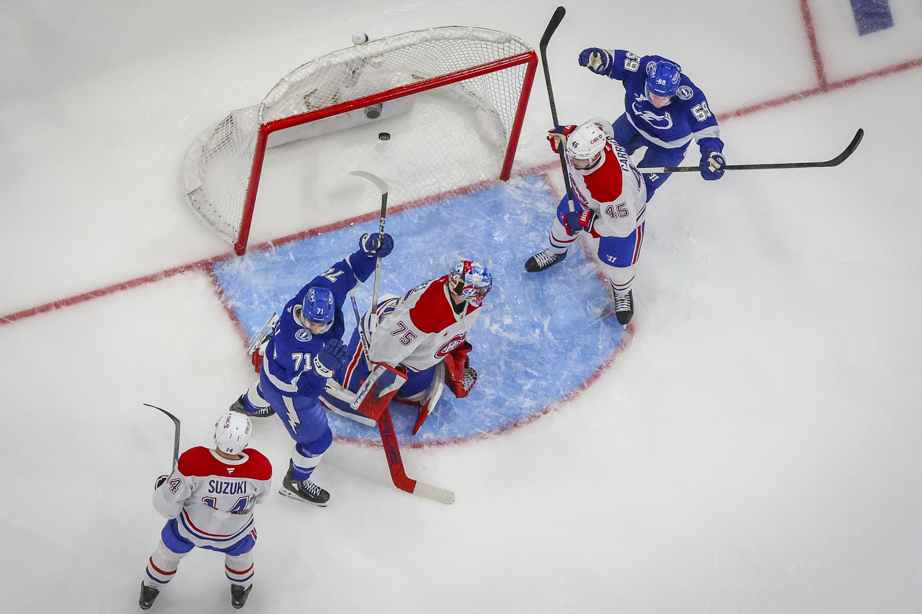 A view from above shows the puck in the net behind a Canadiens goalie on his knees in the crease while two Lightning players raise their arms in celebration.