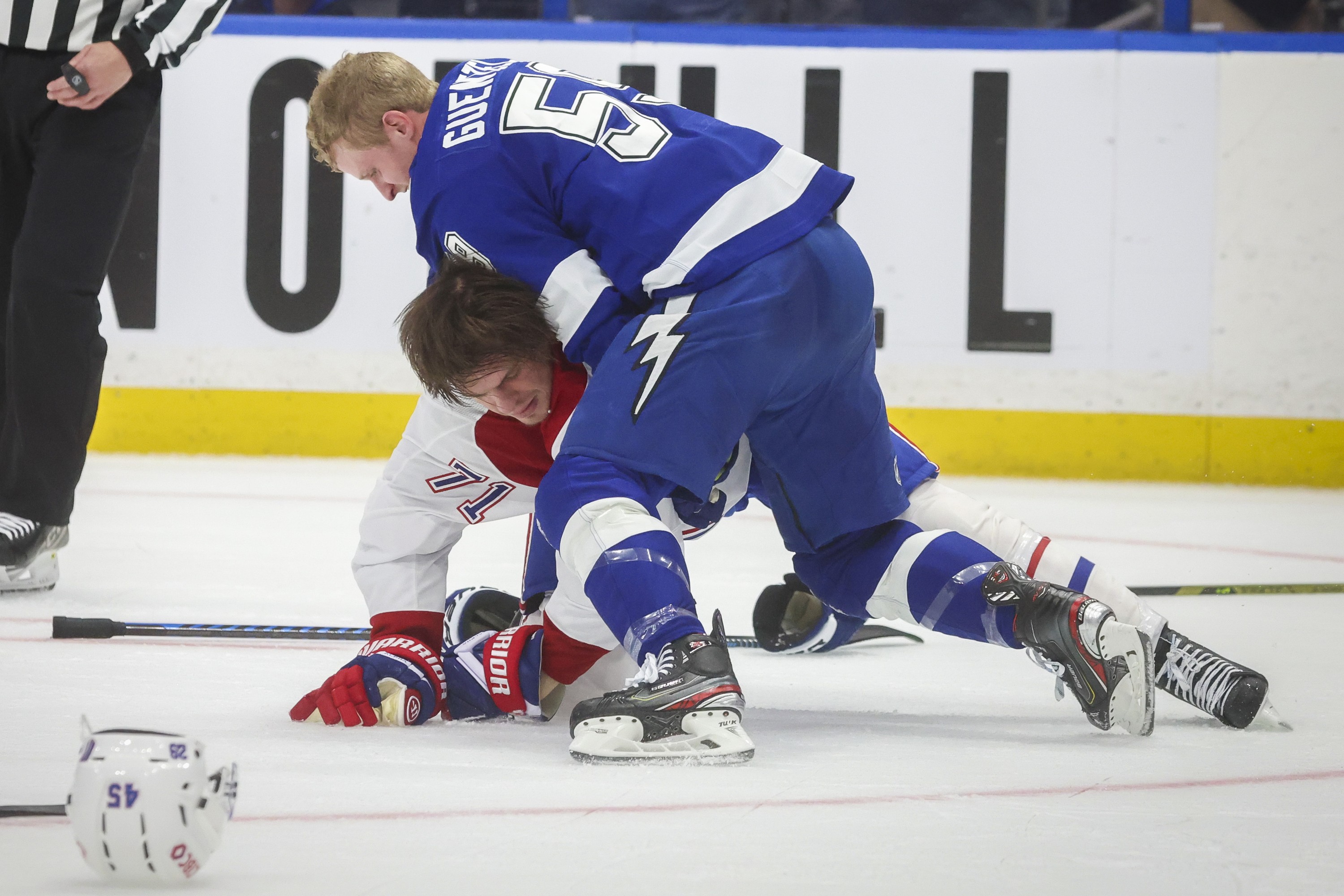 Tampa Bay Lightning's Jake Guentzel (59) holds down Canadiens centre Jake Evans on the ice, neither of them wearing a helmet.