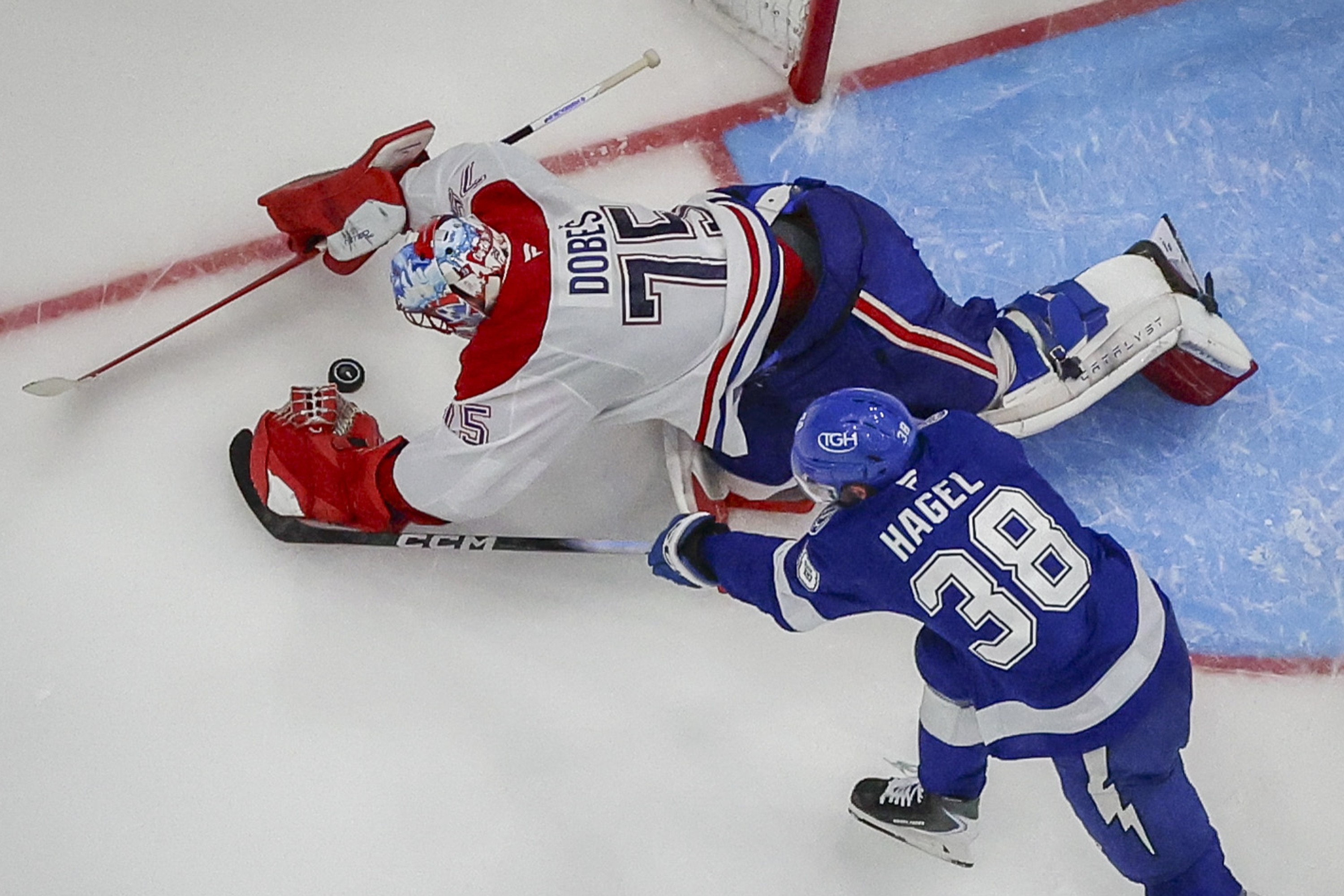 Canadiens goaltender Jakub Dobes (75) dives on the loose puck as Tampa Bay Lightning left wing Brandon Hagel (38) attempts to poke at the puck 