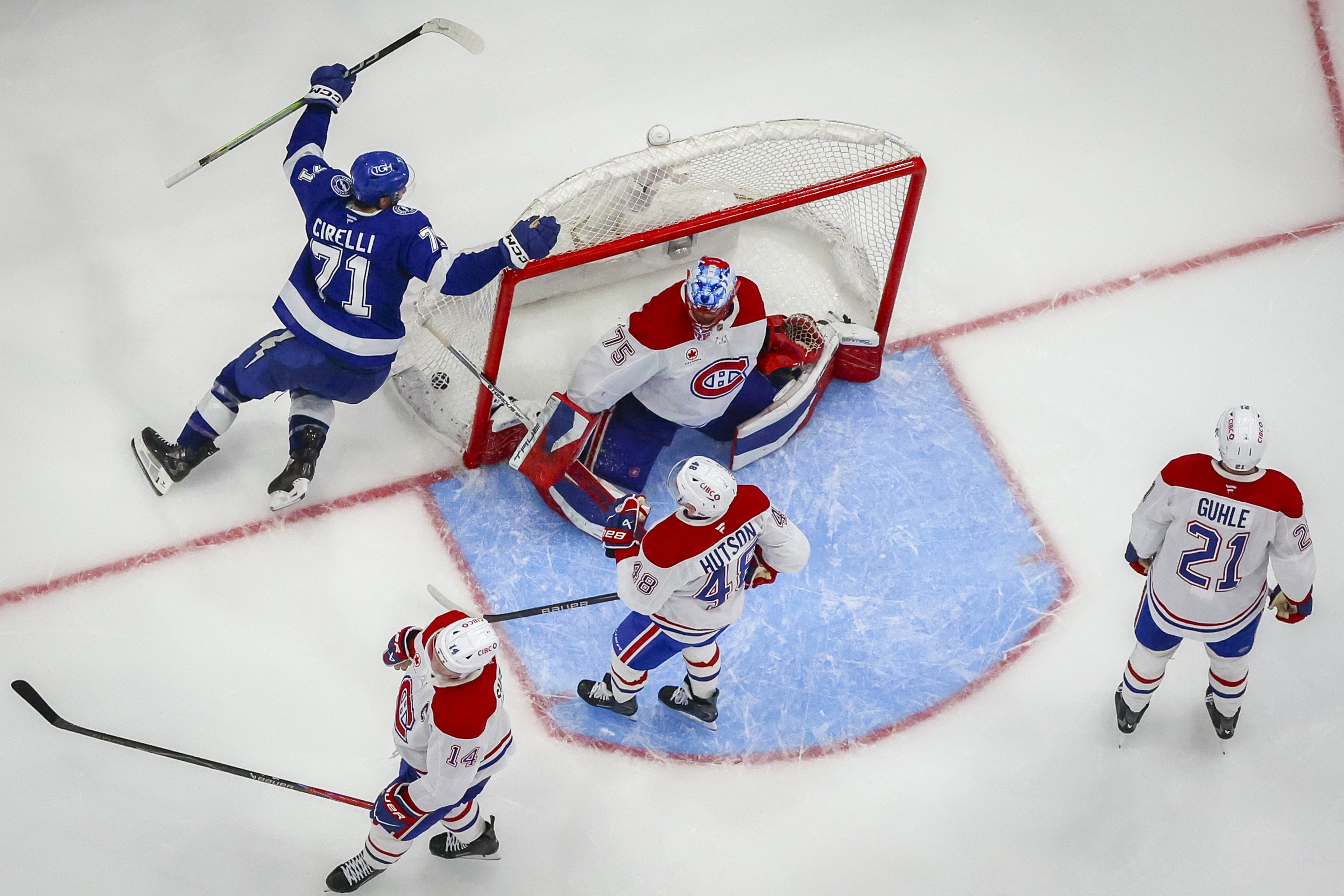 Tampa Bay Lightning's Anthony Cirelli raises his arms in celebration as the puck is seen in the net behind the Canadiens goaltender in a view from above.