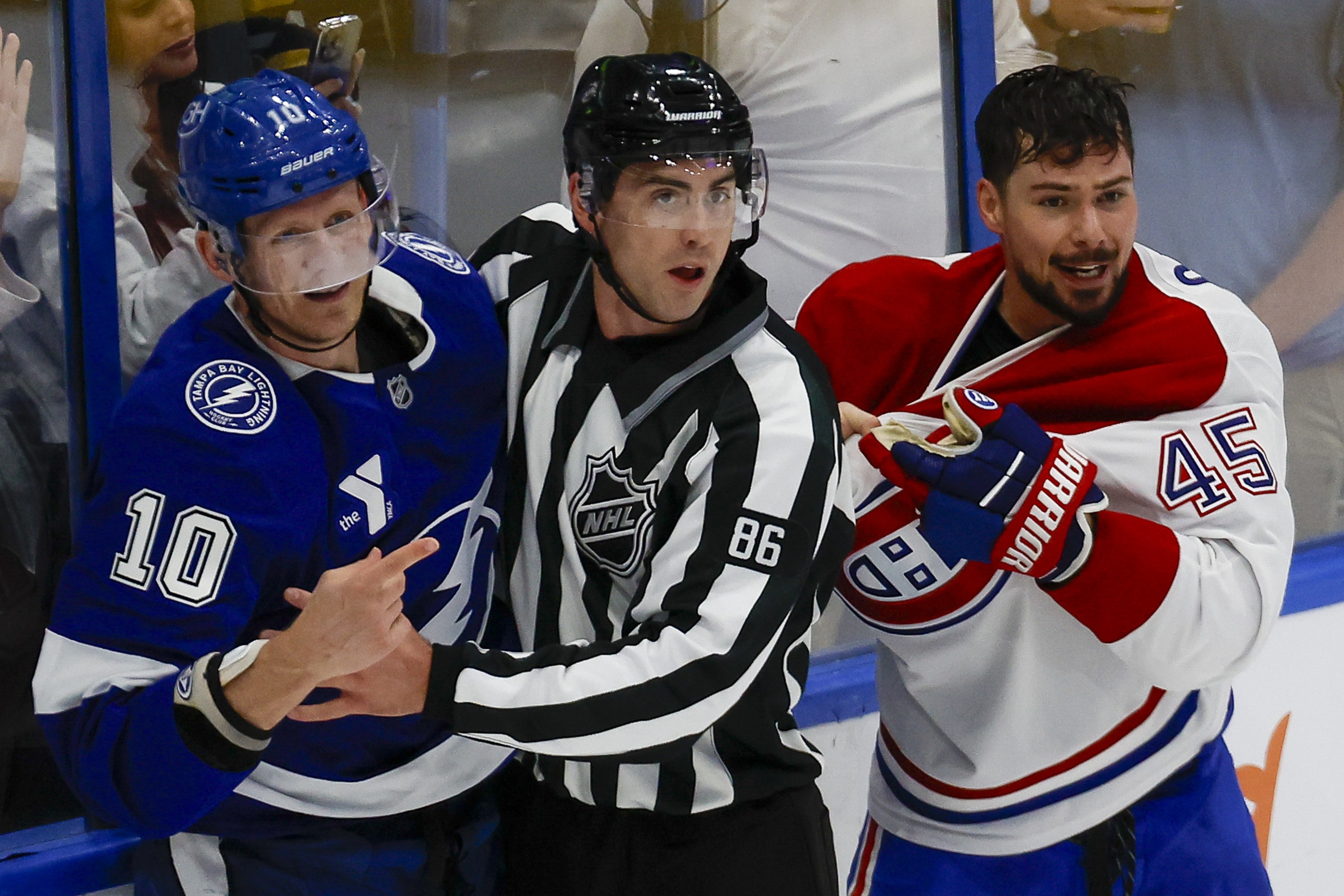 A linesman stands between Lightning's Corey Perry and Canadiens' Alexandre Carrier along the boards.
