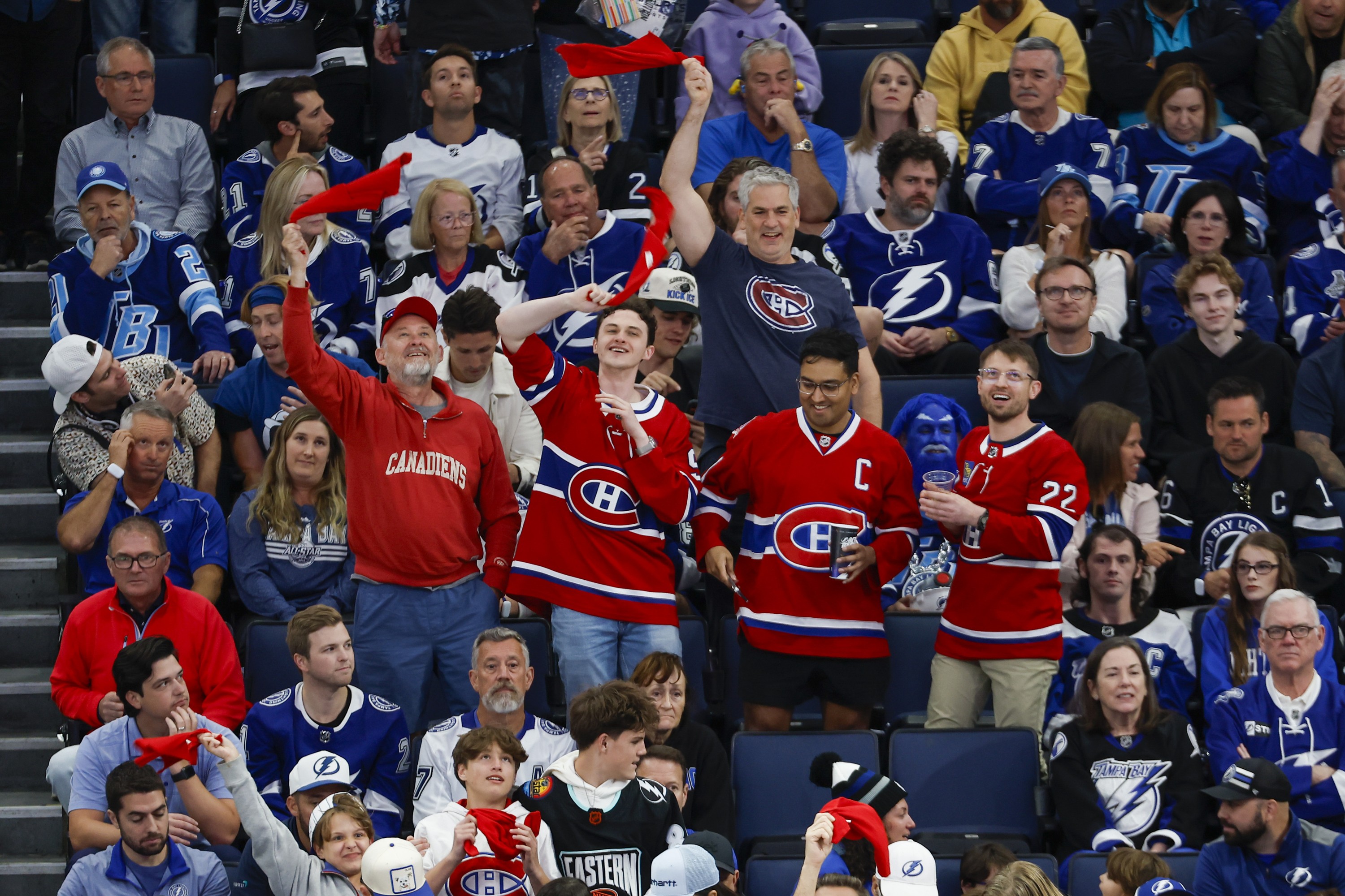 People wearing clothes with Canadiens logos celebrate surrounded by people wearing Tampa Bay Lightning clothes in the stands.