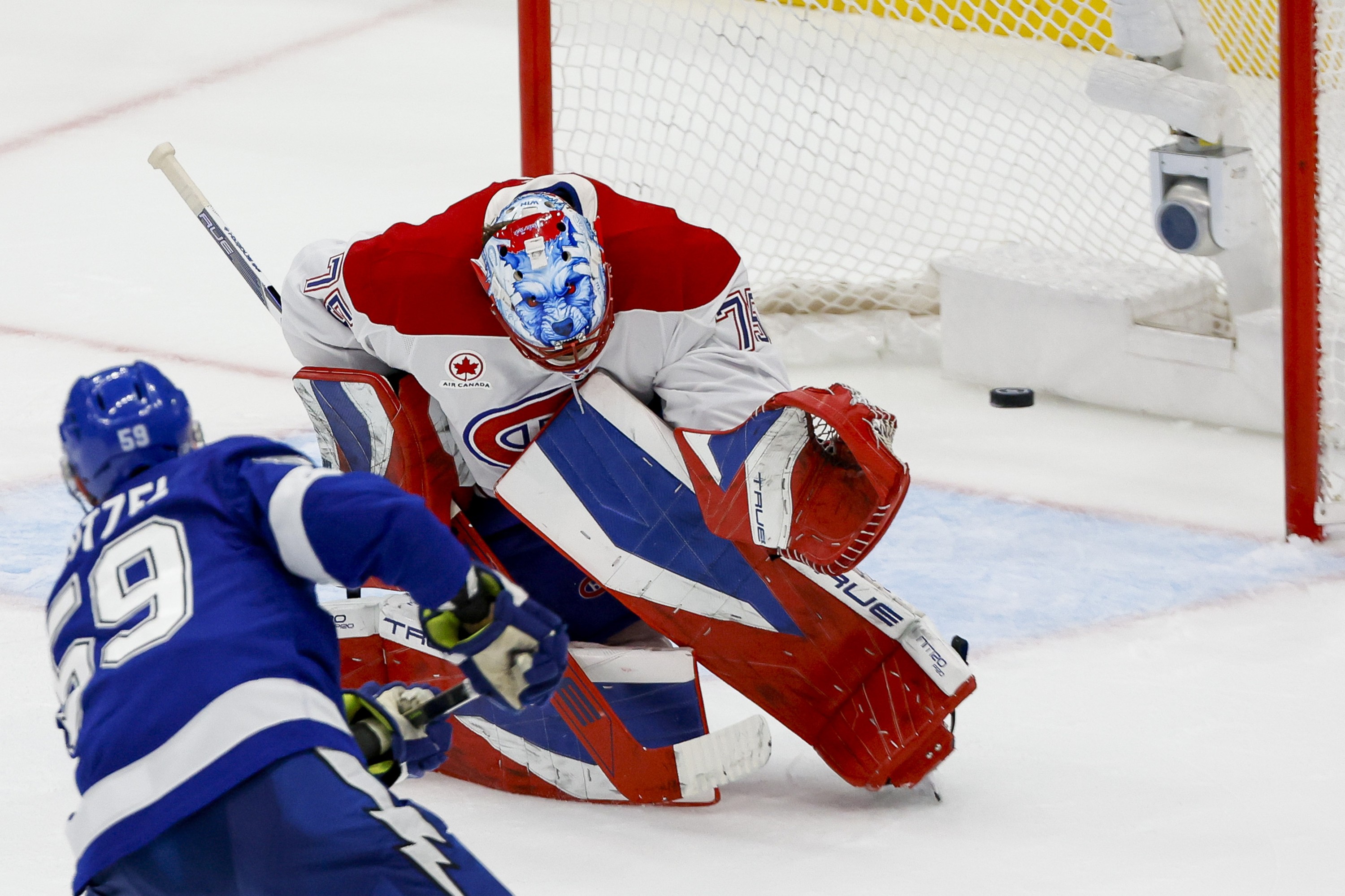 The puck is mid-air heading toward the net as Canadiens goaltender Jakub Dobes tries to block and Lightning's Jake Guentzel follows through on a shot.