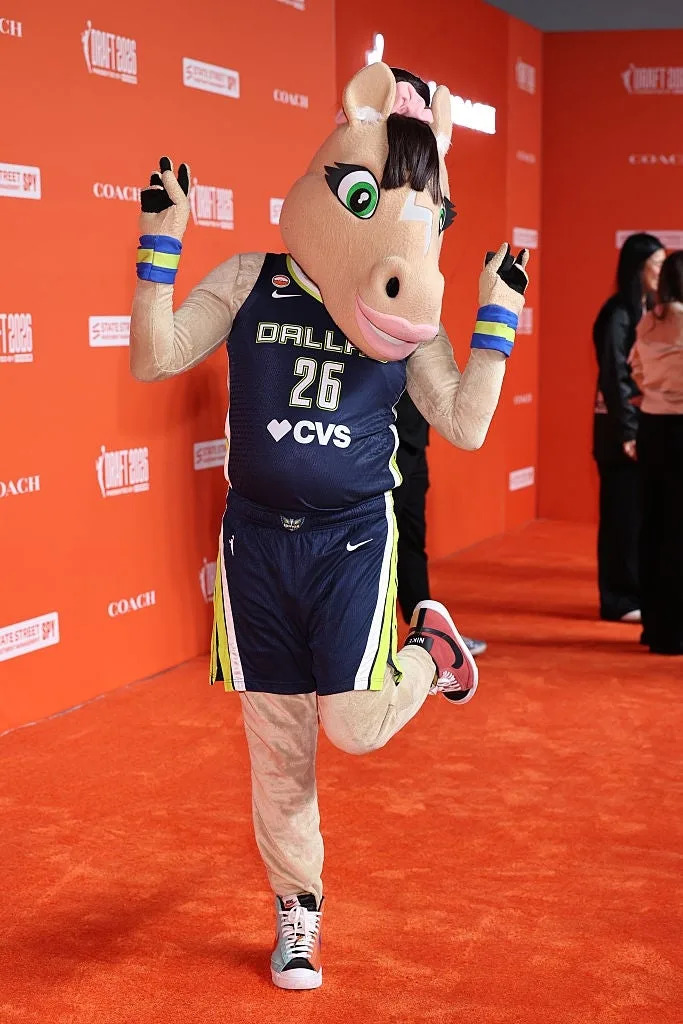 Mascot posing playfully on the red carpet in a basketball uniform with "Dallas 26" and "CVS" text