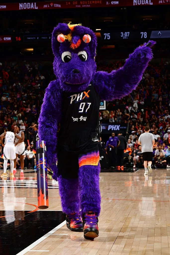 Mascot in a purple furry outfit with a basketball uniform, entertaining a crowd during a basketball game