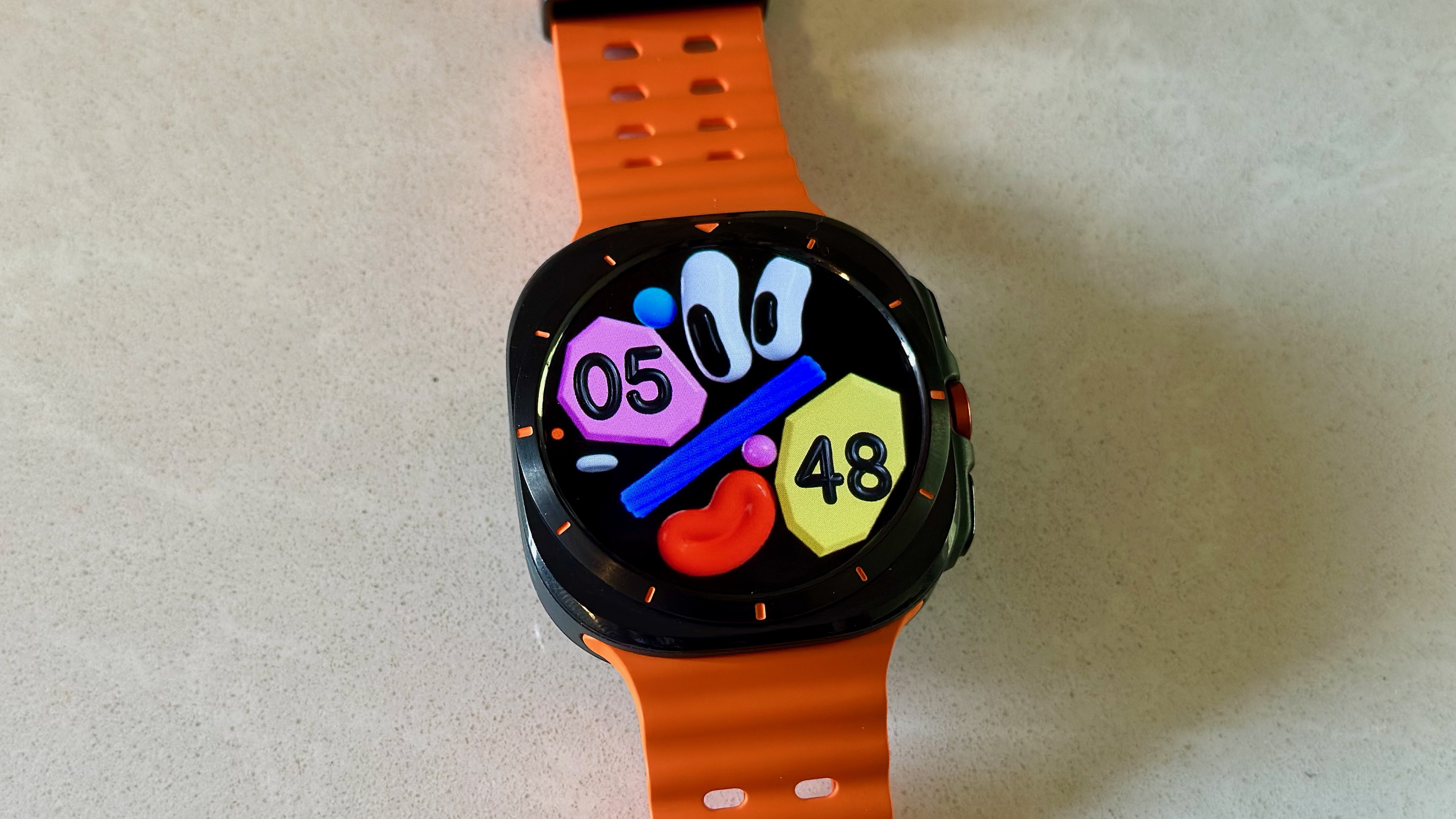 The Samsung Galaxy Watch Ultra sitting on a white counter, showing the Funny Faces watch face.