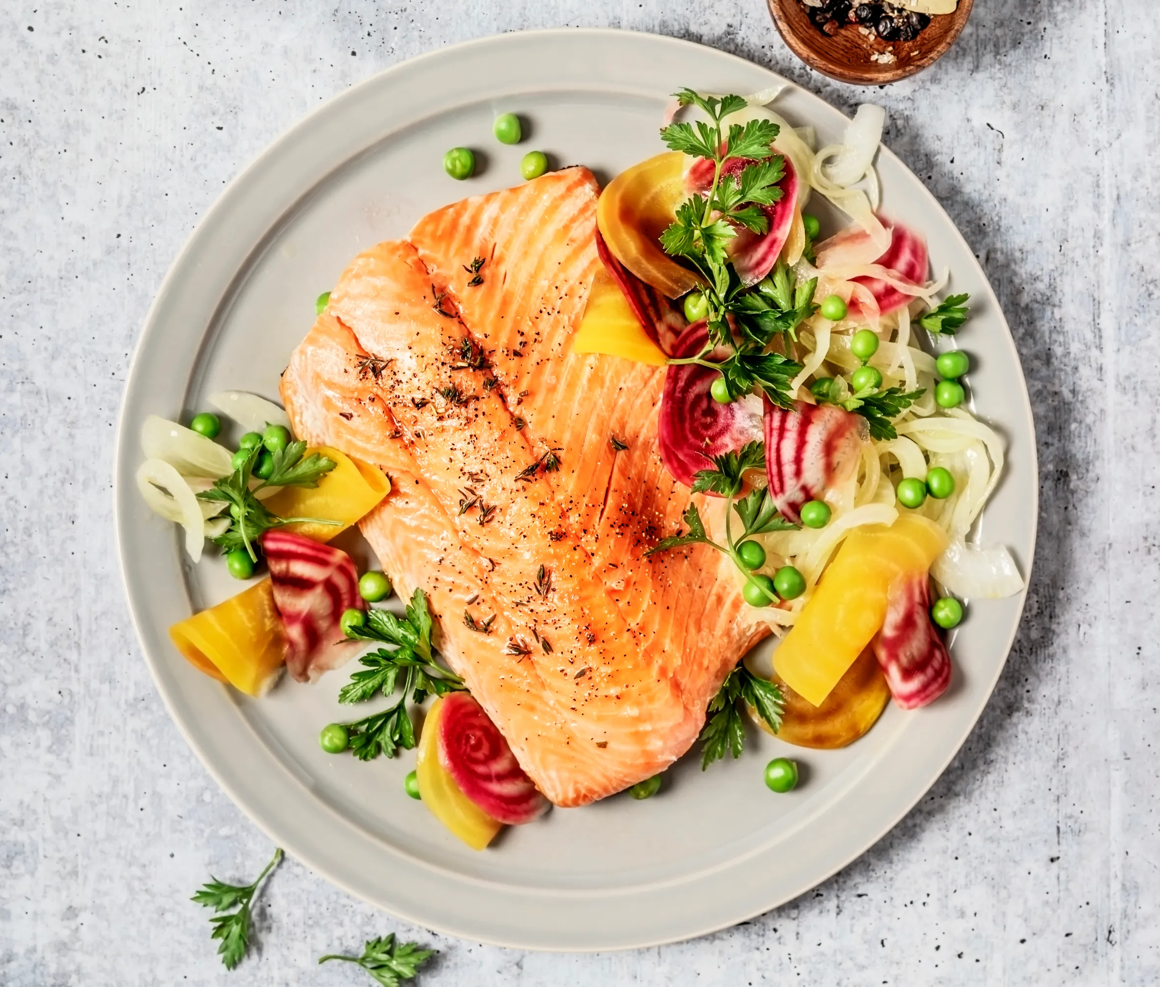 Pan-fried salmon with vegetables on a gray background.