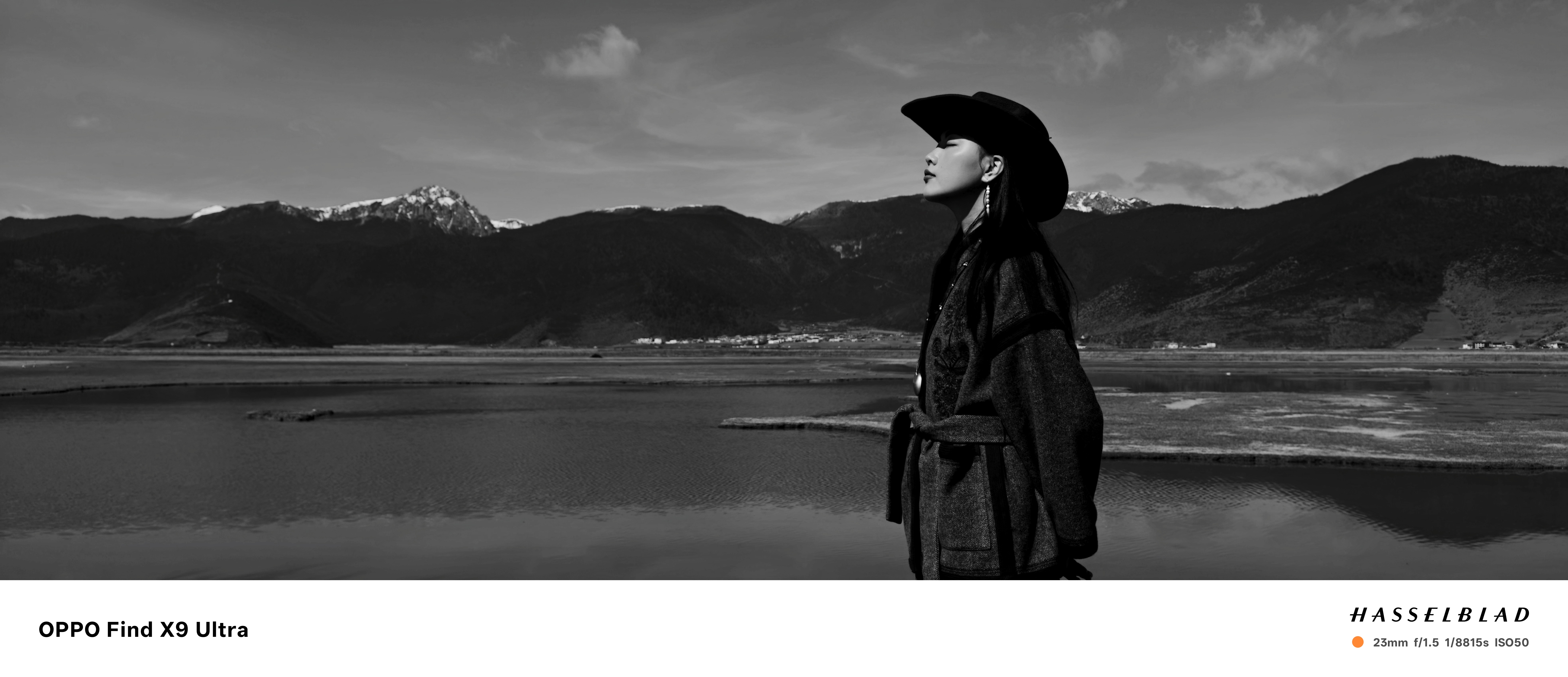 A woman in cowboy hat in front of a snowy mountain with lake, black and white