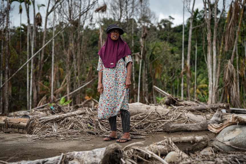 A photo of Salmawati standing amid rubble and smashed down trees.