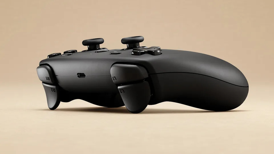 A promotional image of the Steam Controller, seen from the front and side. It is a charcoal black gamepad, laid on a beige surface and background.