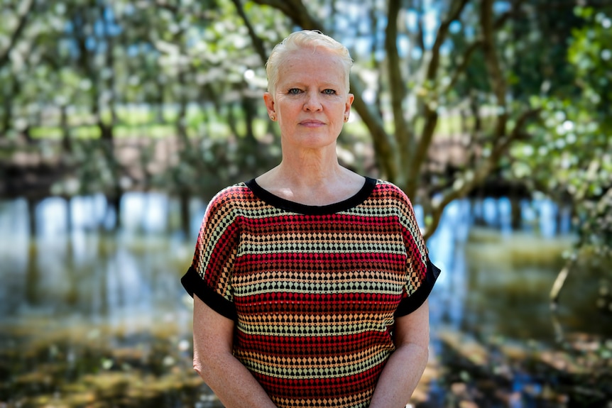 Cr Raffan wearing a patterned shirt stands in front of Cooks River with trees overhead.