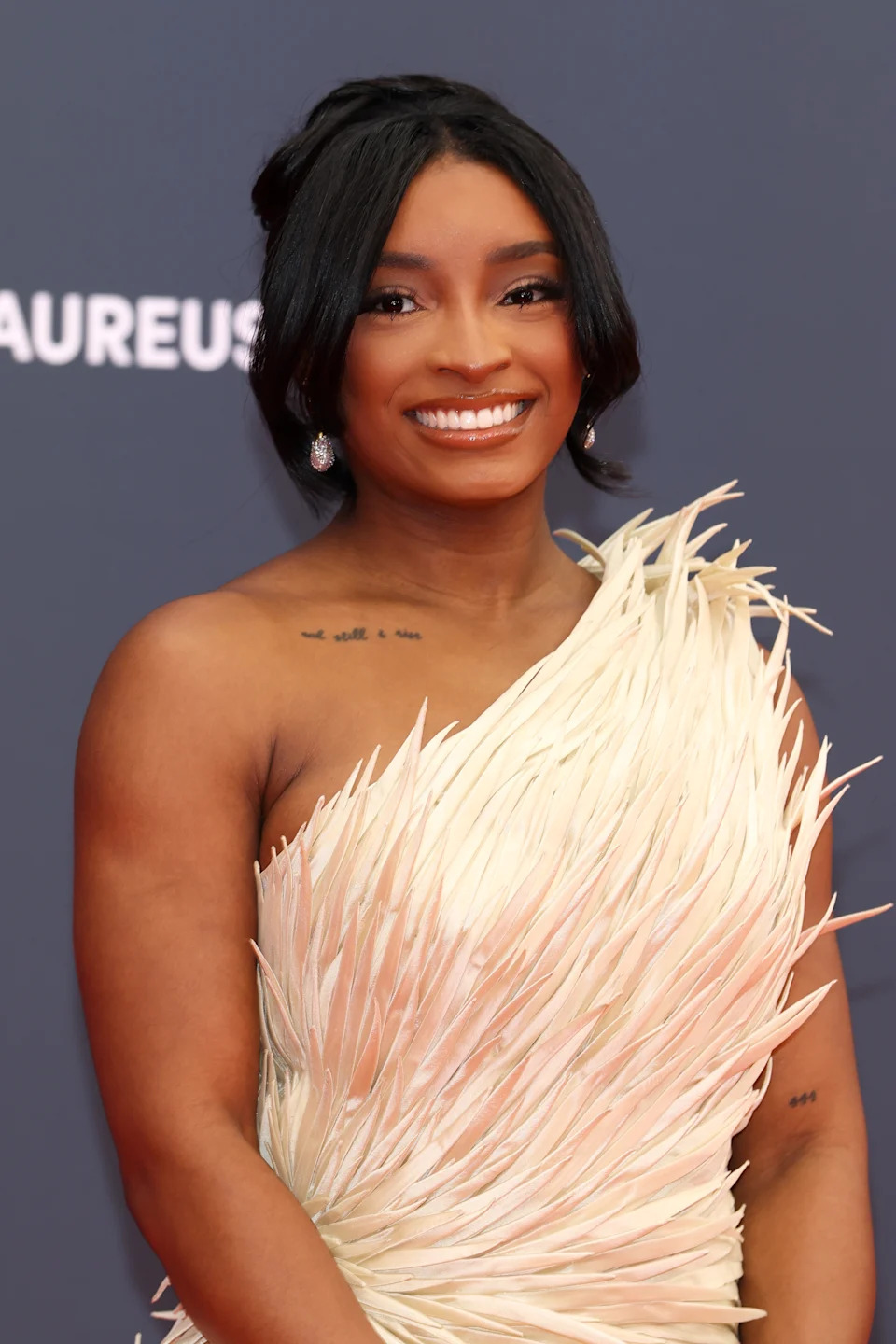 Person wearing a stylish, textured off-shoulder gown, smiling at a formal event