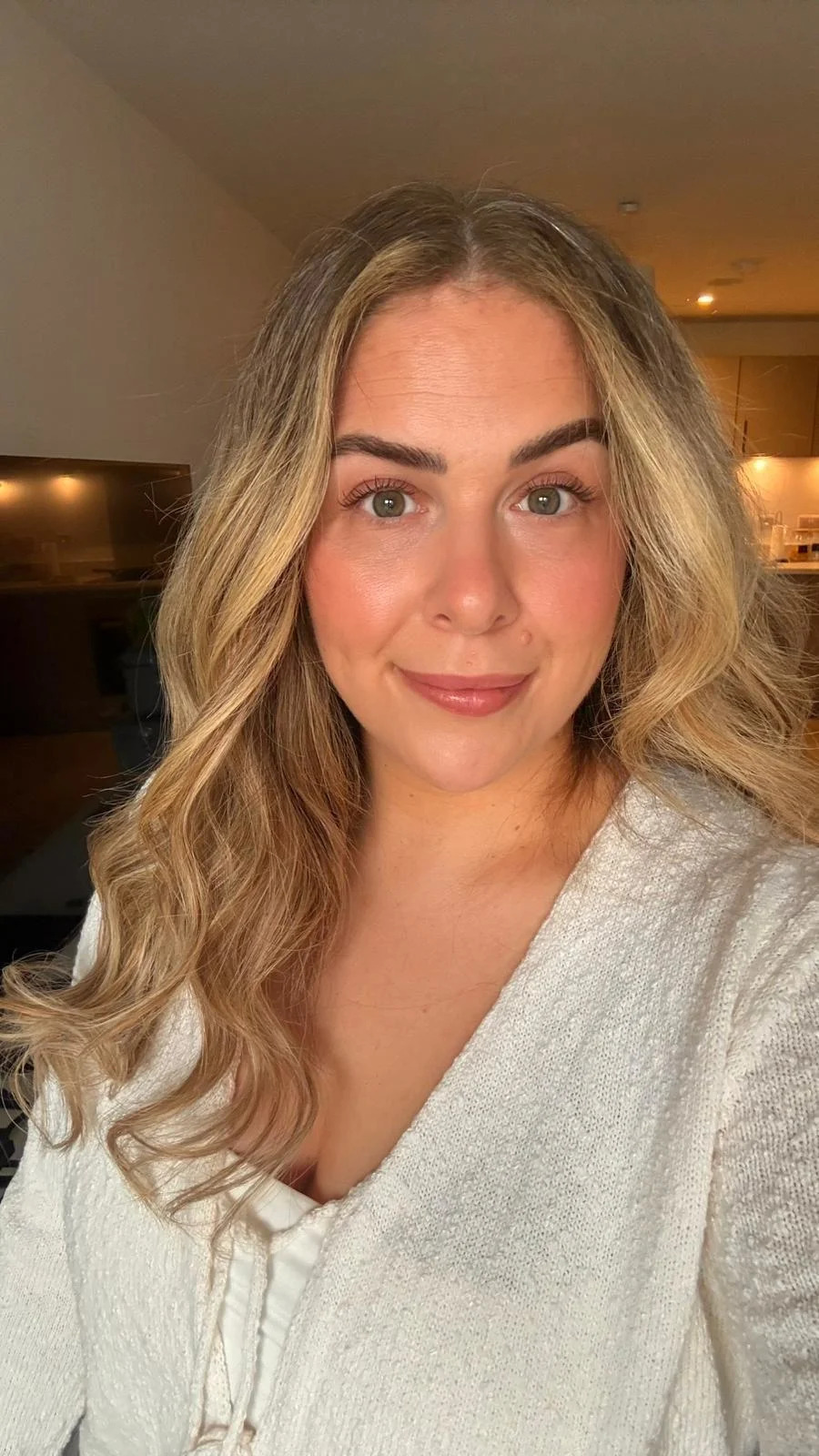 Photo of a lady with long blonde hair wearing a white top. She is smiling.