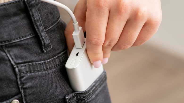 A person inserting a power bank into a pocket of their jeans.