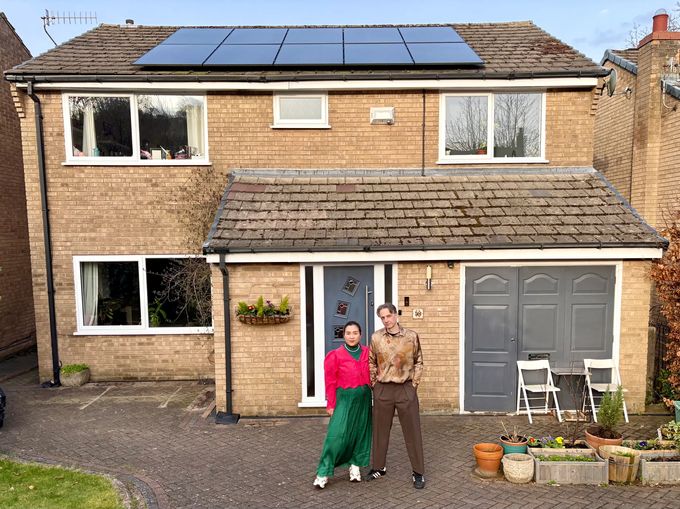 Two people standing in front of a brick house with solar panels on the roof.