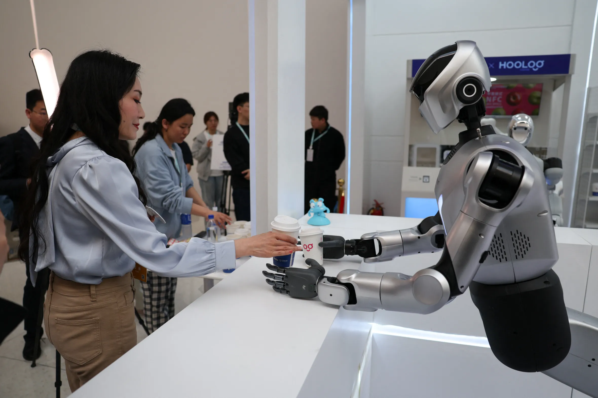 A Kuavo-5W humanoid robot passes a cup of coffee to a journalist.