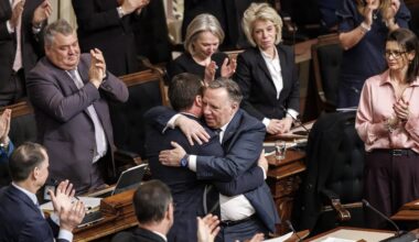 François Legault hugs Simon Jolin-Barrette as MNAs at their desks around them applaud.