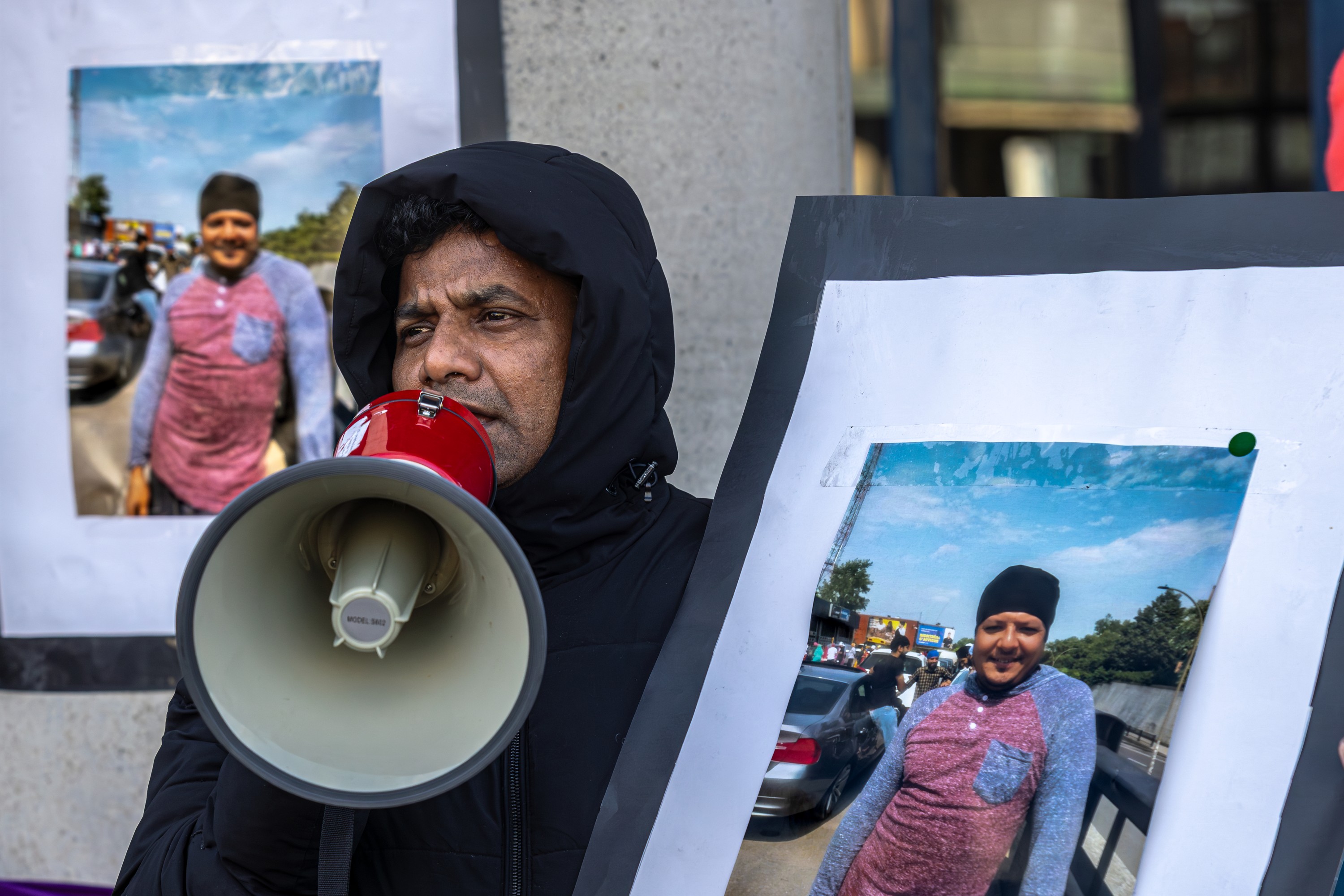 A man holds a megaphone and stands next to a photo of an unhoused man.