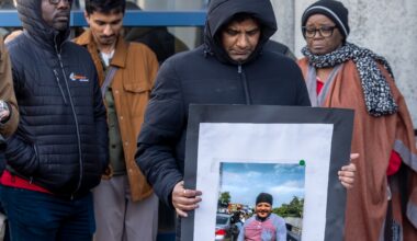 Four people stand with heads bowed. One man is holding a photo of an unhoused man.