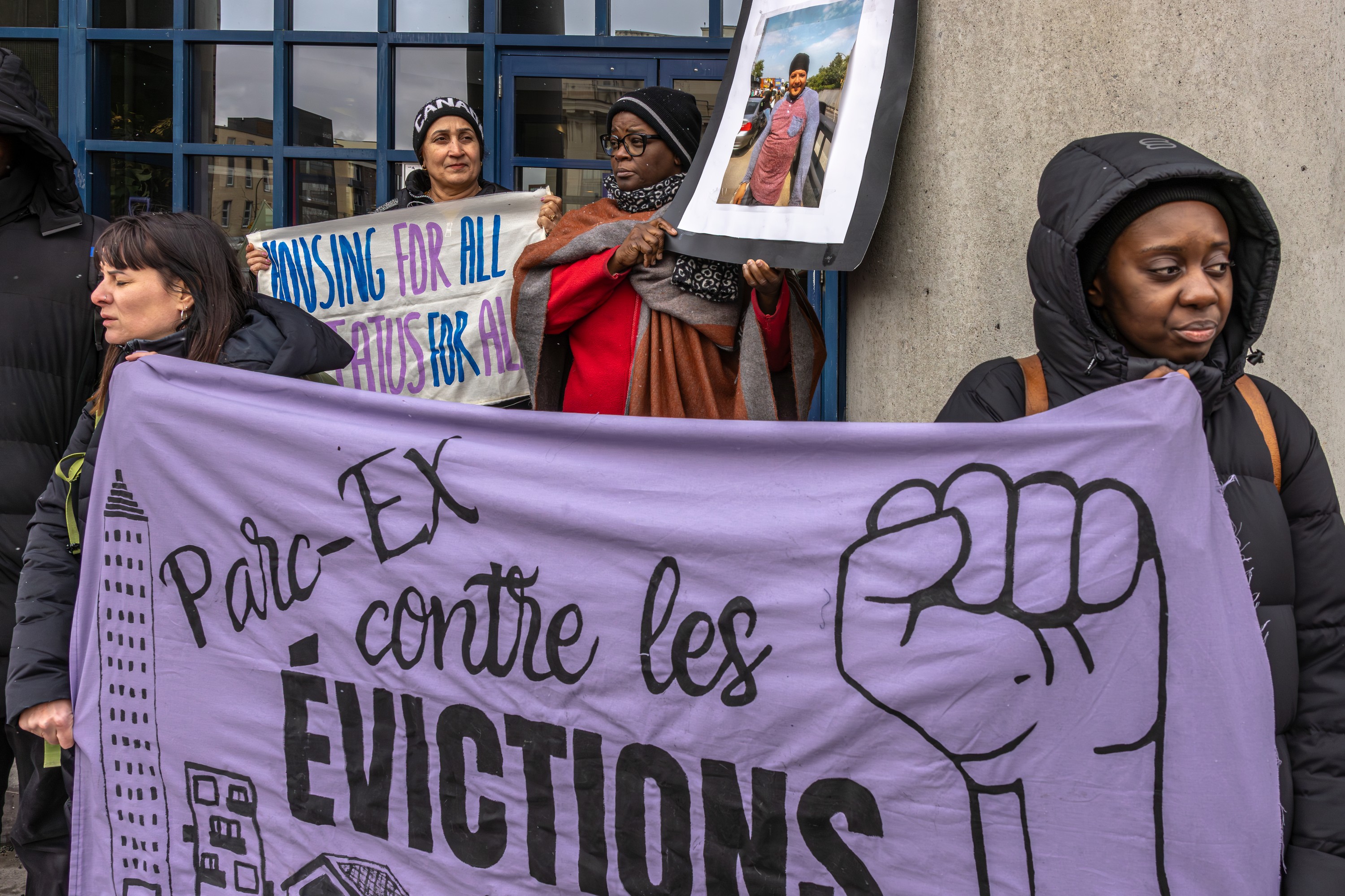 Four women hold a banner that says Parc-Ex contre les evictions. One of them is holding a photo of a man.