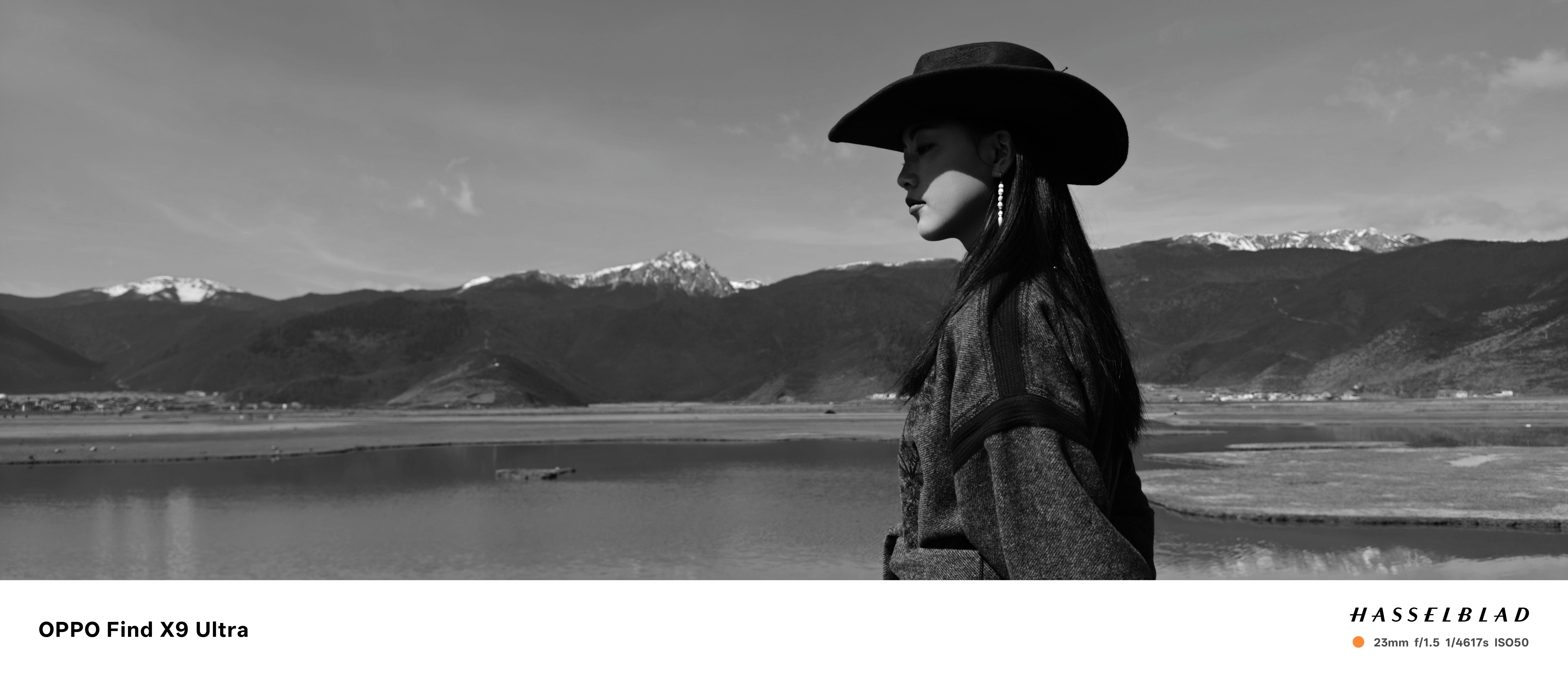 A woman in cowboy hat in front of a snowy mountain with lake, black and white