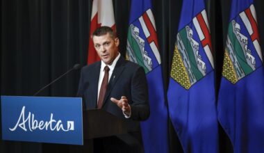 Alberta Finance Minister speaks at a lectern during a news conference, with Canadian and Albertan flags behind him.