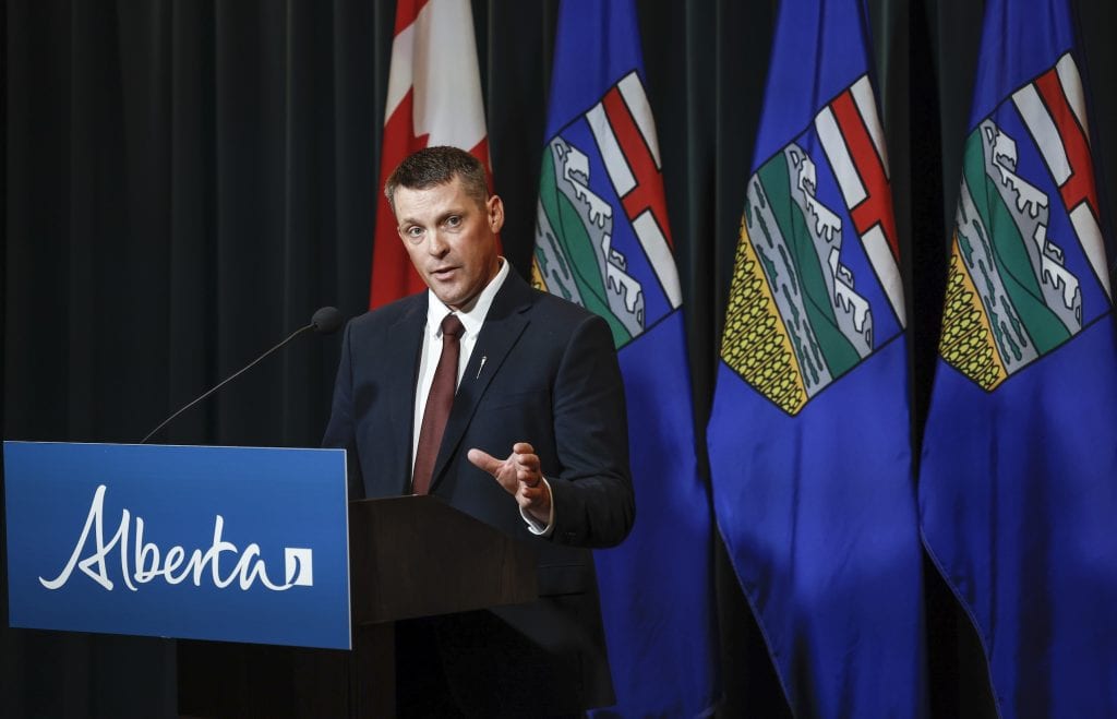 Alberta Finance Minister speaks at a lectern during a news conference, with Canadian and Albertan flags behind him.