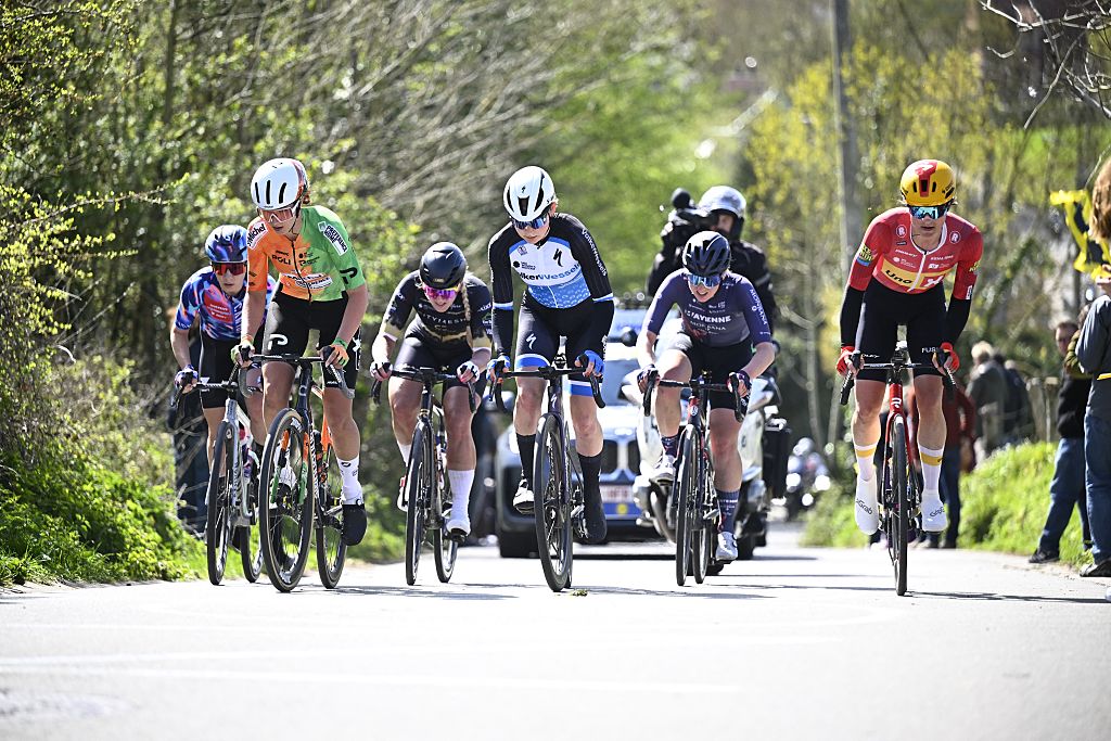 Six riders spread across the road ahead of team cars and camera motorbike