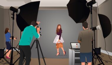 A woman poses in front of a gray backdrop in a photo studio, surrounded by large lights, a camera on a tripod, a photographer, an assistant, and a person at a laptop displaying her image.