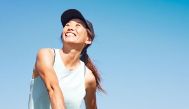 Happy woman wearing sports cap and top playing tennis in the sunshine