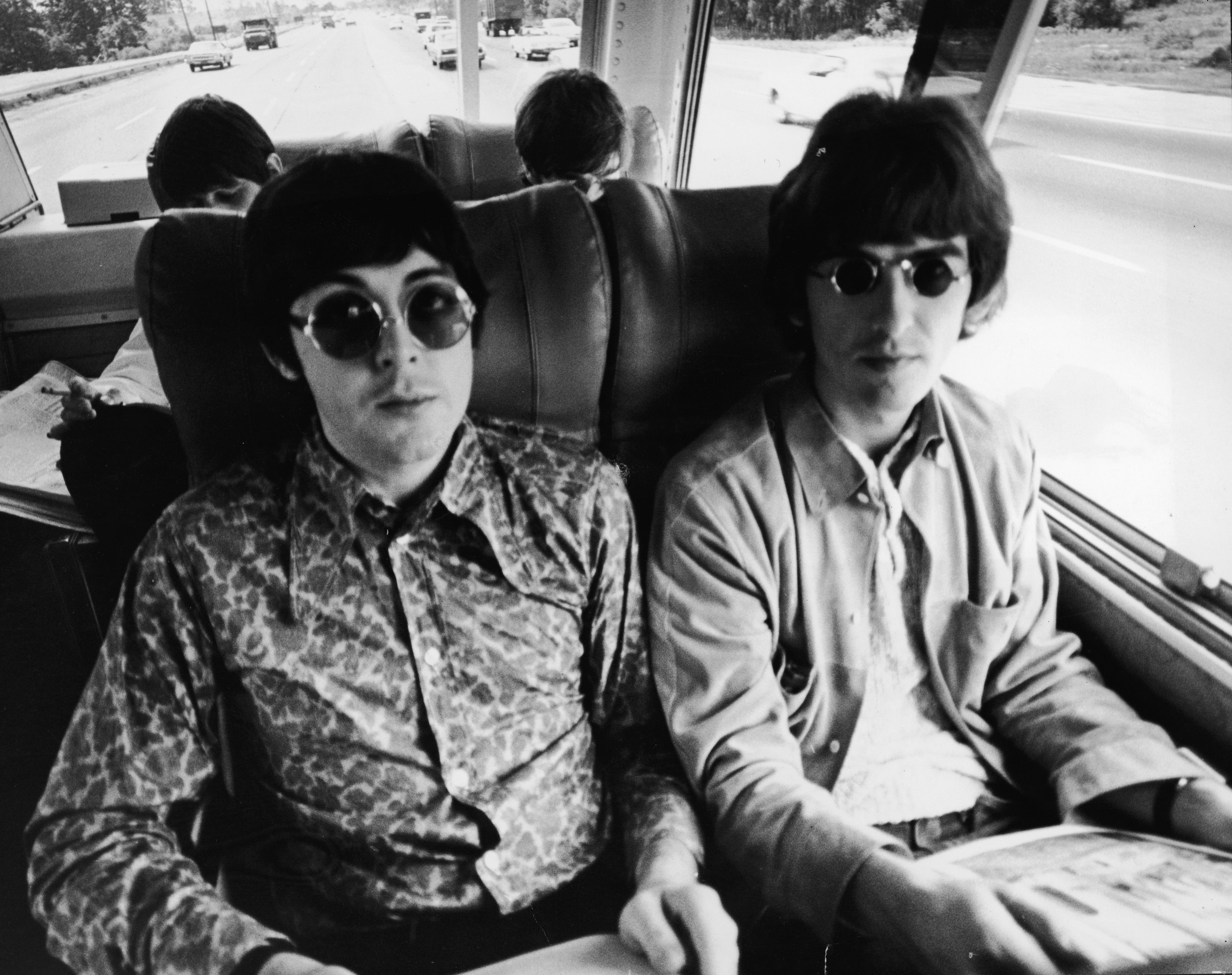 Paul McCartney (left) and George Harrison sit next to each other on their tour bus during a Beatles American tour, c. 1966