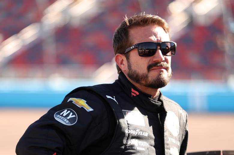 JJ Yeley wearing a black racing suit and sunglasses at a NASCAR track before a race