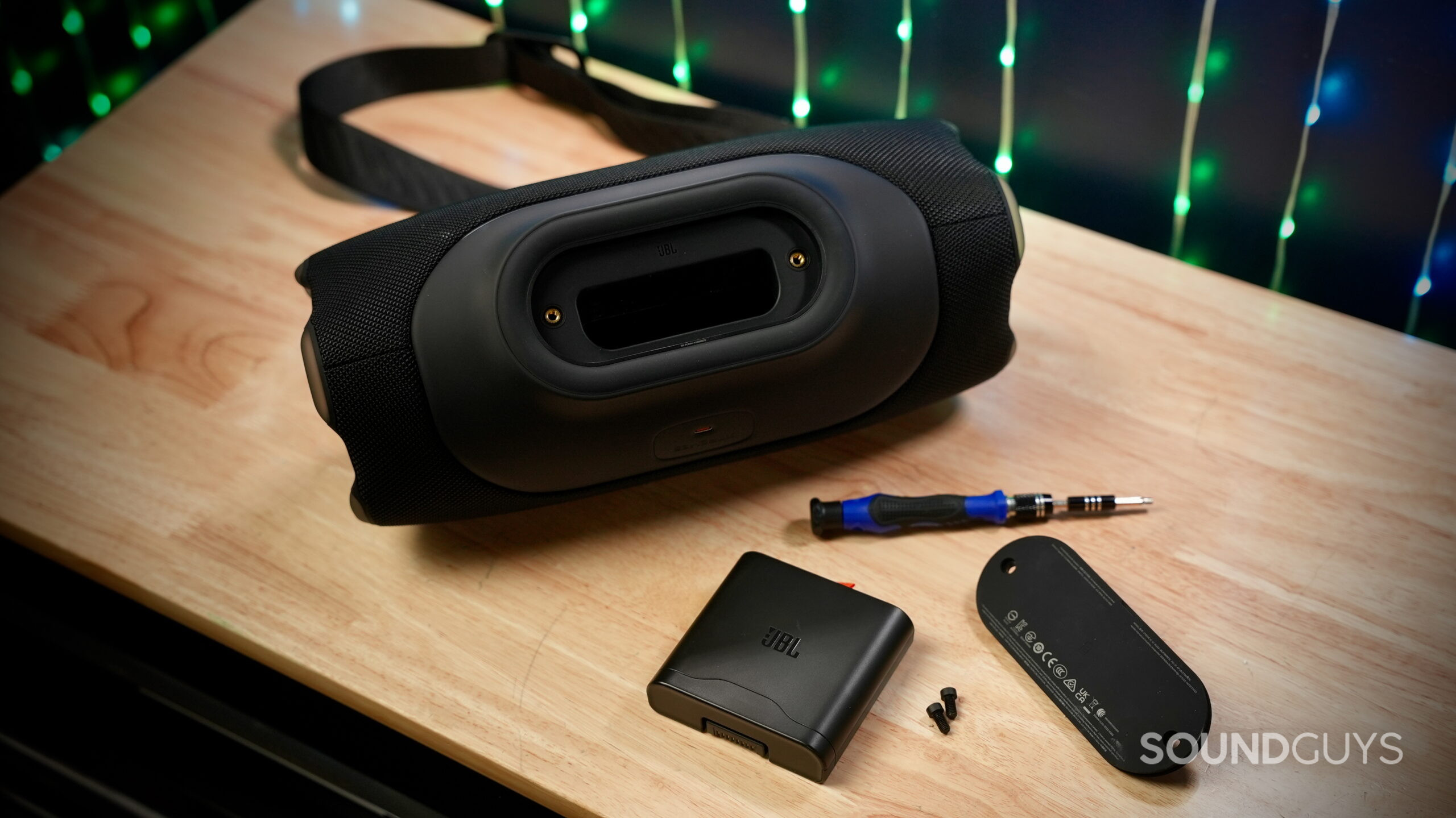 JBL Xtreme 5 with removable battery pack and tools laid out on a wooden table.
