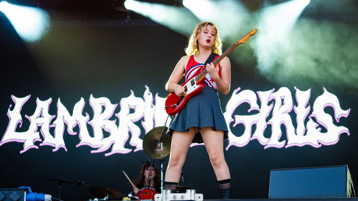 Phoebe Lunny of Lambrini Girls singing into a microphone while performing onstage.