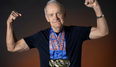 Senior man with arms raised wearing multiple gold medals around his neck, the blue ribbons read &ldquo;San Diego Senior Games&rdquo;