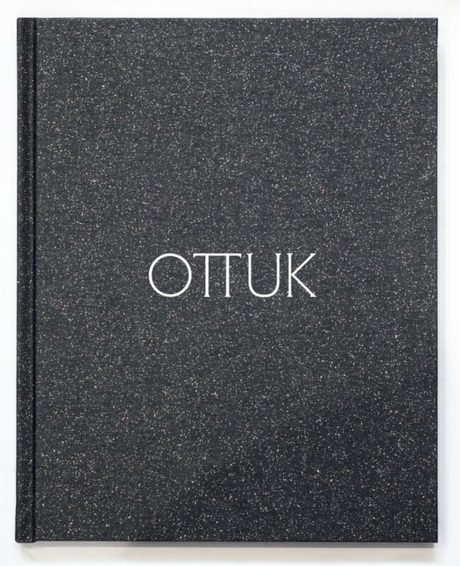 A black book cover with a subtle speckled texture features the word "OTTUK" in large, white, uppercase letters centered on the front.