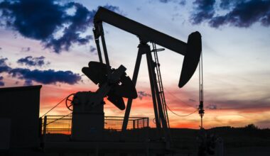 The image shows the silhouette of a pumpjack drawing out oil from a well head against an orange sunset.