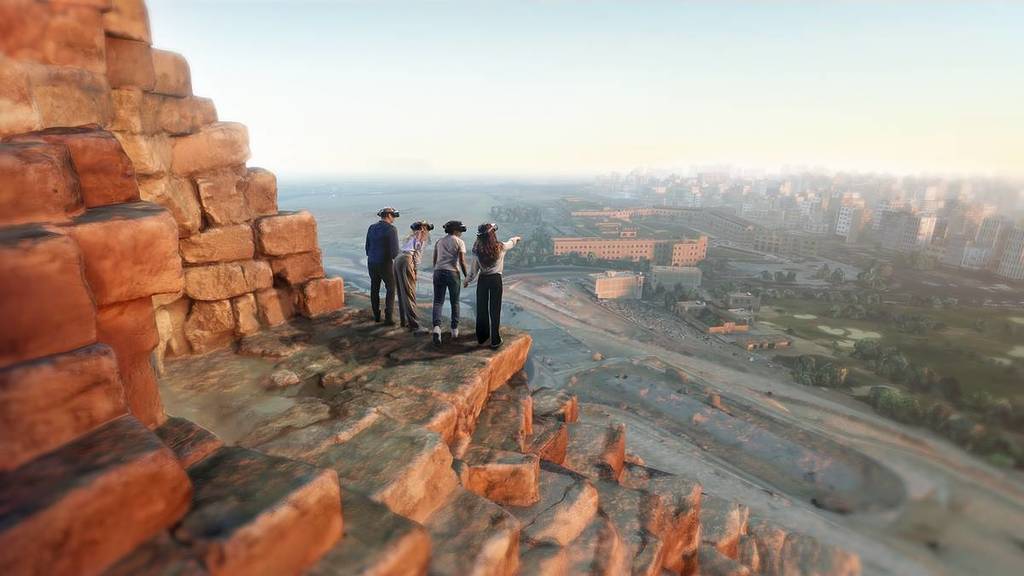 four people wearing VR headsets stand of the edge of a digitally rendders pyramid and gaze out at the Giza Plateau at The Horizon of Khufu VR experience