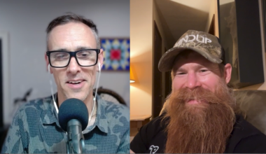 A split-screen image featuring two men smiling at the camera. The man on the left has short, gray hair, wears glasses, and a patterned shirt, speaking into a microphone with earphones. The man on the right has a long red beard, wears a camouflage baseball cap, and is seated in a well-lit indoor space with a cozy ambiance.