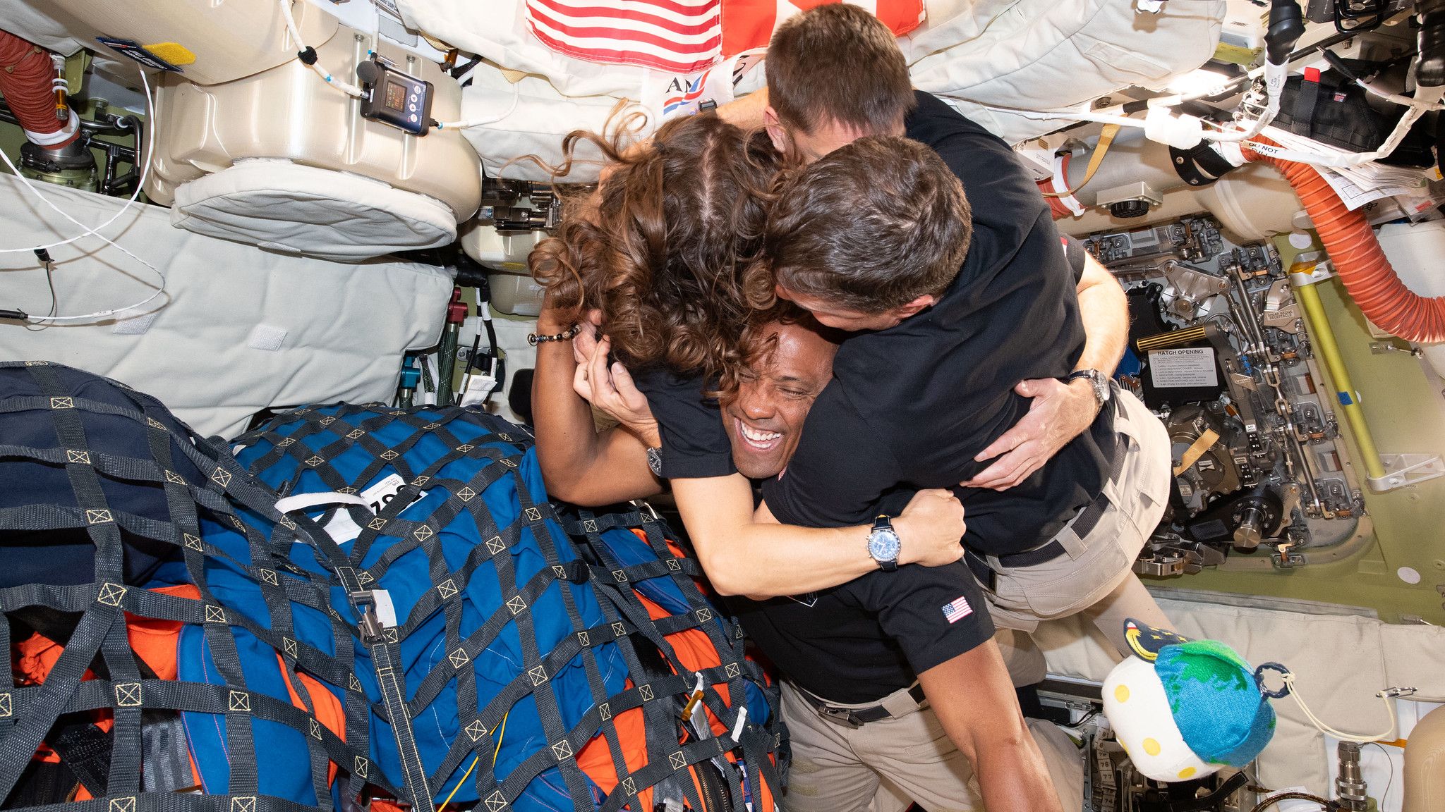 Four astronauts hug as they float in microgravity in a space capsule.