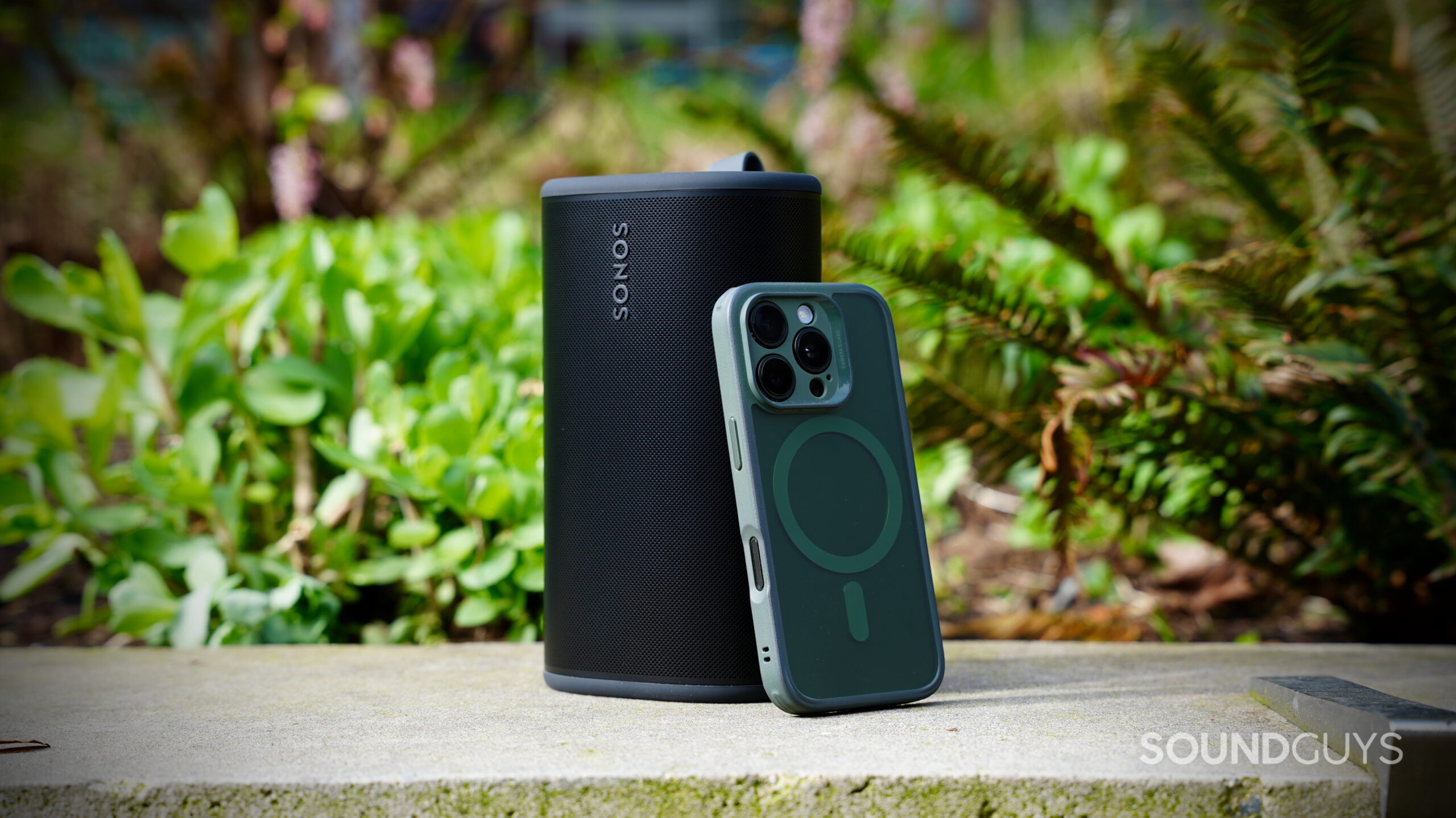 The Sonos Play portable speaker standing outdoors next to a smartphone for size comparison.