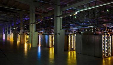 A large data center with rows of illuminated server racks and numbered concrete pillars under dim, colored lighting.
