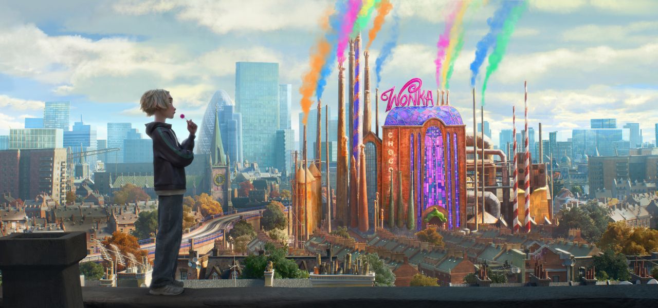 An animated blonde-haired boy stands on a rooftop looking toward a vibrant, whimsical Wonka chocolate factory that emits colorful smoke into a city skyline.